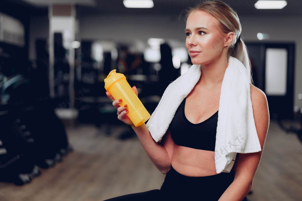 年轻年轻的运动型女人在运动后在健身房喝一杯毛巾营养人