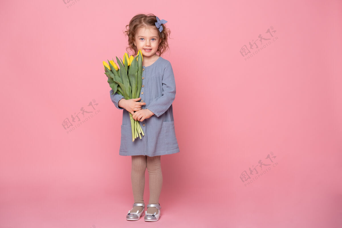 新鲜美丽的金发小女孩穿着蓝色的裙子 粉色背景上有一束黄色郁金香 还有文字空间女孩花搞笑
