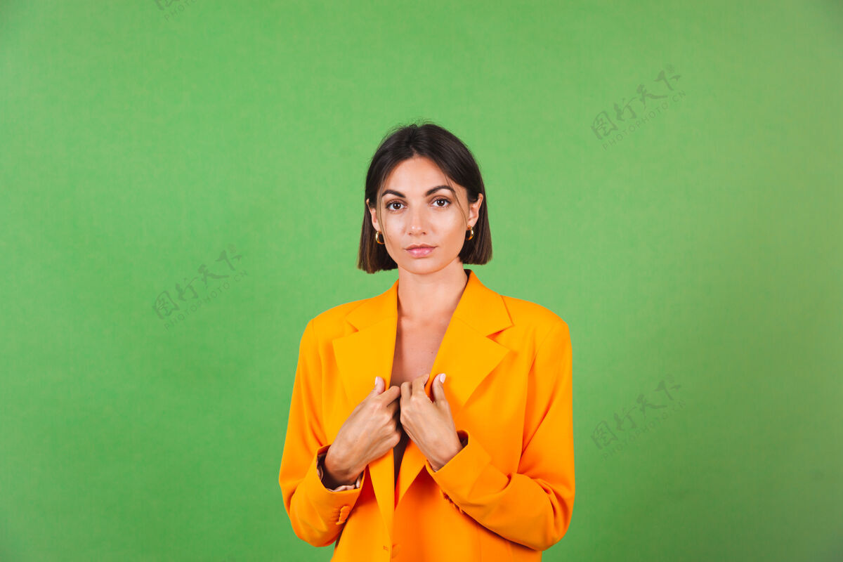 女人穿着丝绸米色连衣裙和橙色超大西装的时尚女士 身着绿色 带着积极的情绪微笑长成人西装