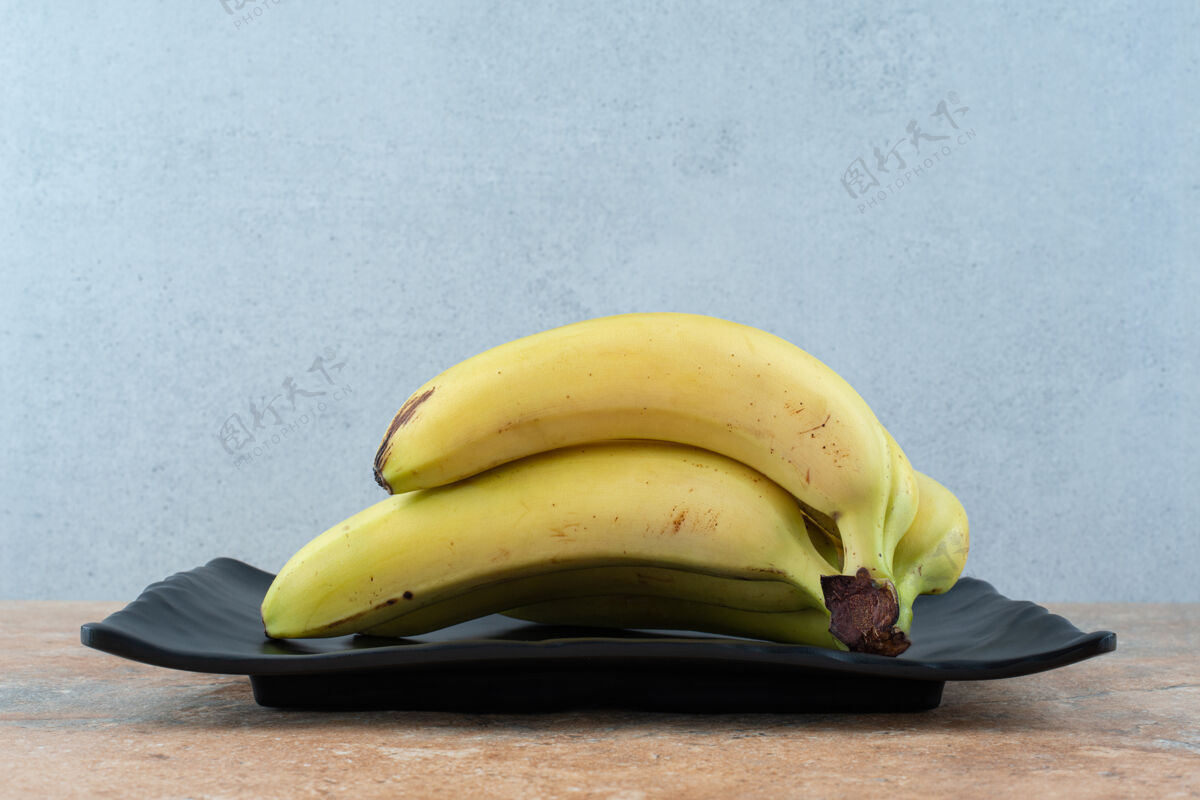 黄一个黑色的盘子里装满了成熟的水果香蕉 放在灰色的盘子里热带果皮香蕉
