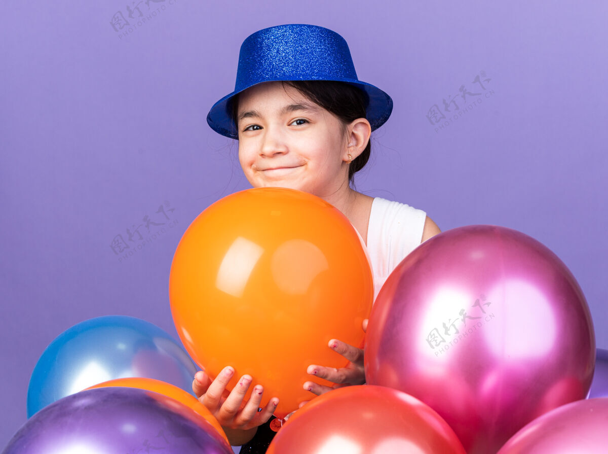 拜托年轻的高加索女孩戴着蓝色的派对帽 站在紫色的墙上 氦气球与复制空间隔离开来站着年轻的白种人
