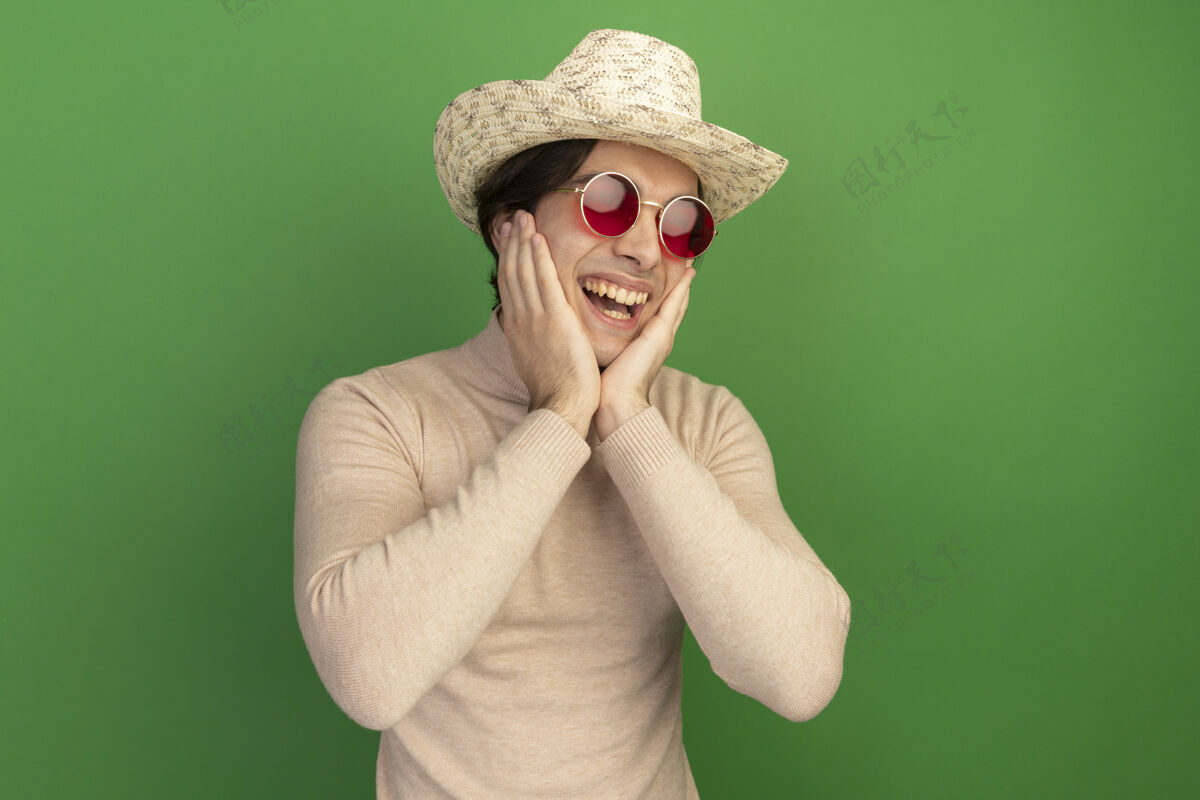 帅哥戴帽子戴眼镜的年轻帅哥-隔离在绿墙上帽子年轻人眼镜