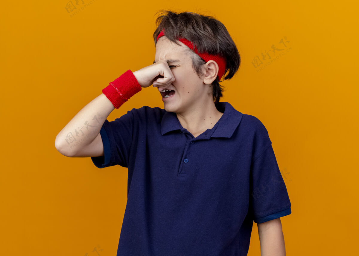 背带哭泣的年轻英俊的运动男孩戴着头带和戴着牙套的腕带擦着橘色墙上孤立的眼泪湿巾姿势脸