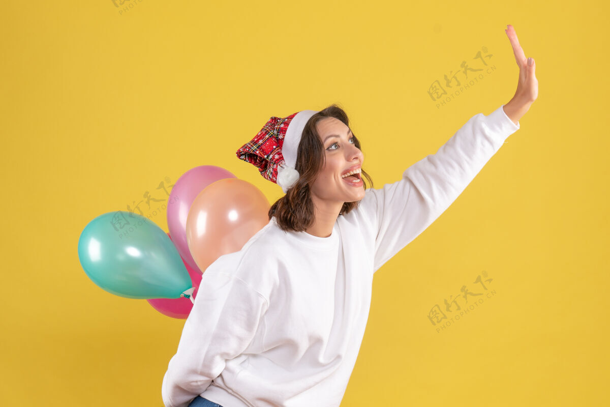 欢呼正面图年轻女性快乐地藏着五颜六色的气球新年圣诞彩色节日女人的情感圣诞节年轻的女性前面