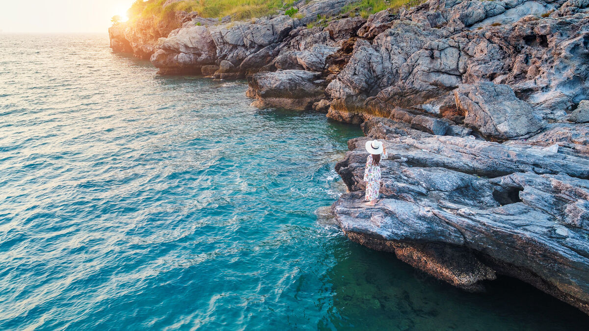 女人站在岩石顶上 望着四长岛的海边和日落的年轻女子悬崖风景女性