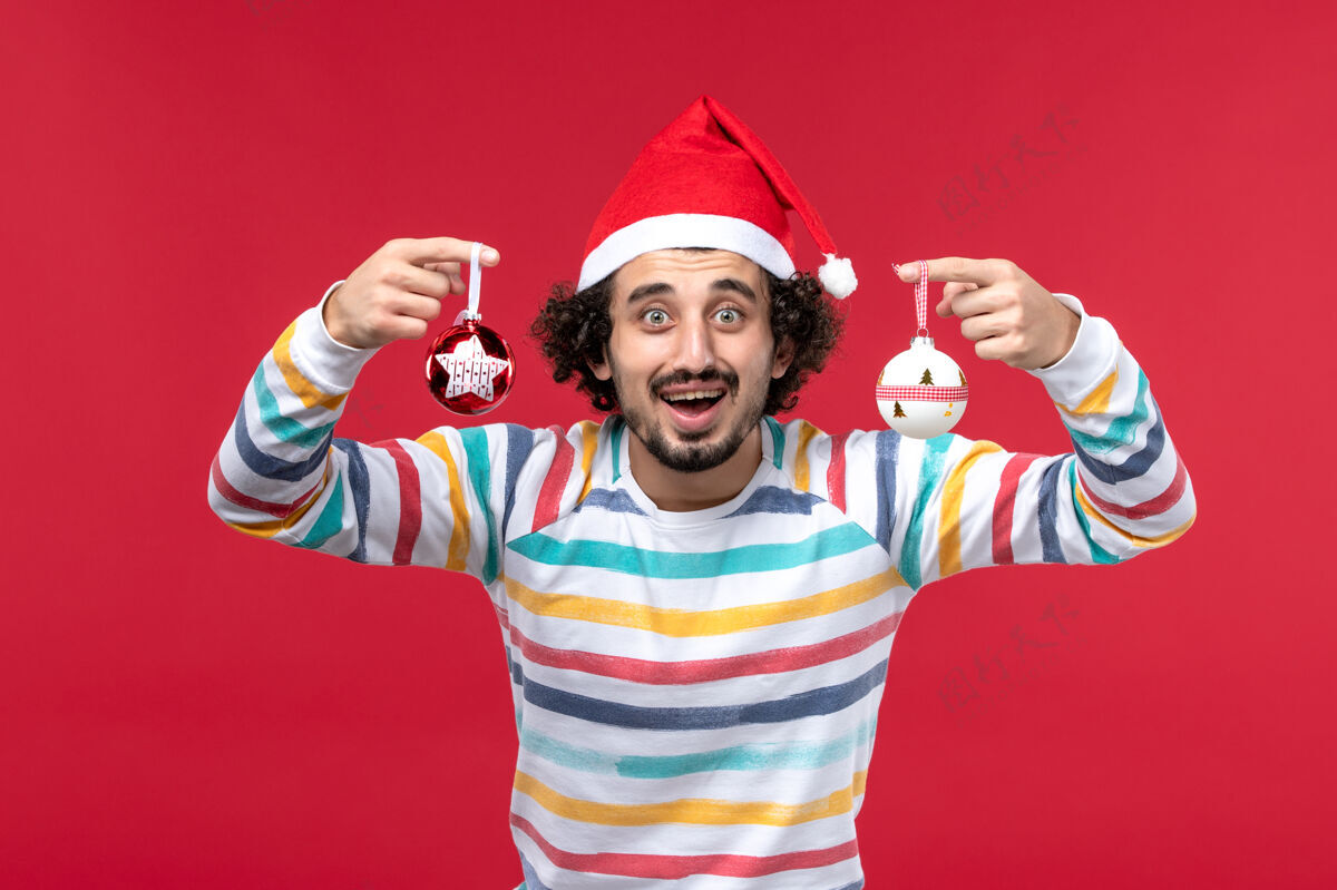人正面图：年轻男子手持圣诞树玩具站在红墙上新年放假快乐成人前面