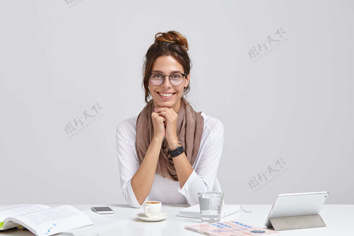 文书容貌开朗的记者 戴着透明眼镜 梳着黑发 边读书边丰富知识 带着温柔的微笑坐在工作台上用触摸板 一杯水商务女性学习平板电脑