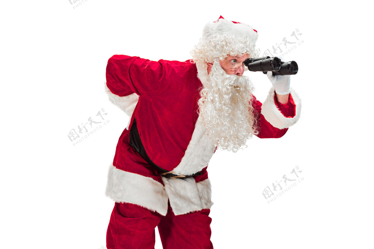 场合一个穿着圣诞老人服装 留着奢华的白胡子 戴着圣诞老人的帽子和一件红色服装的人的肖像——全身都是用望远镜隔离在白色上面的欢乐庆祝欢乐的