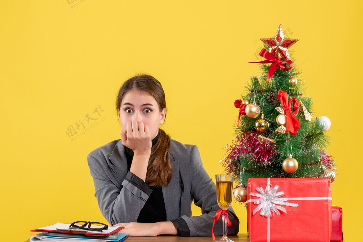 鸡尾酒前视图惊讶的女孩坐在书桌旁把手放在嘴边圣诞树和礼物鸡尾酒桌子导演成人