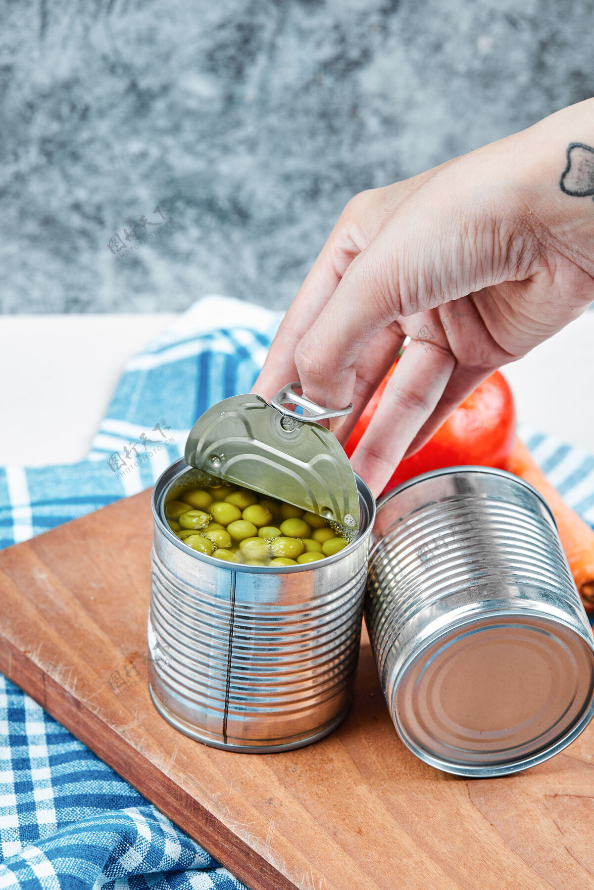 西红柿手拿一罐煮青豌豆放在一张白色的桌子上 桌子上放着蔬菜和桌布大理石滋补手