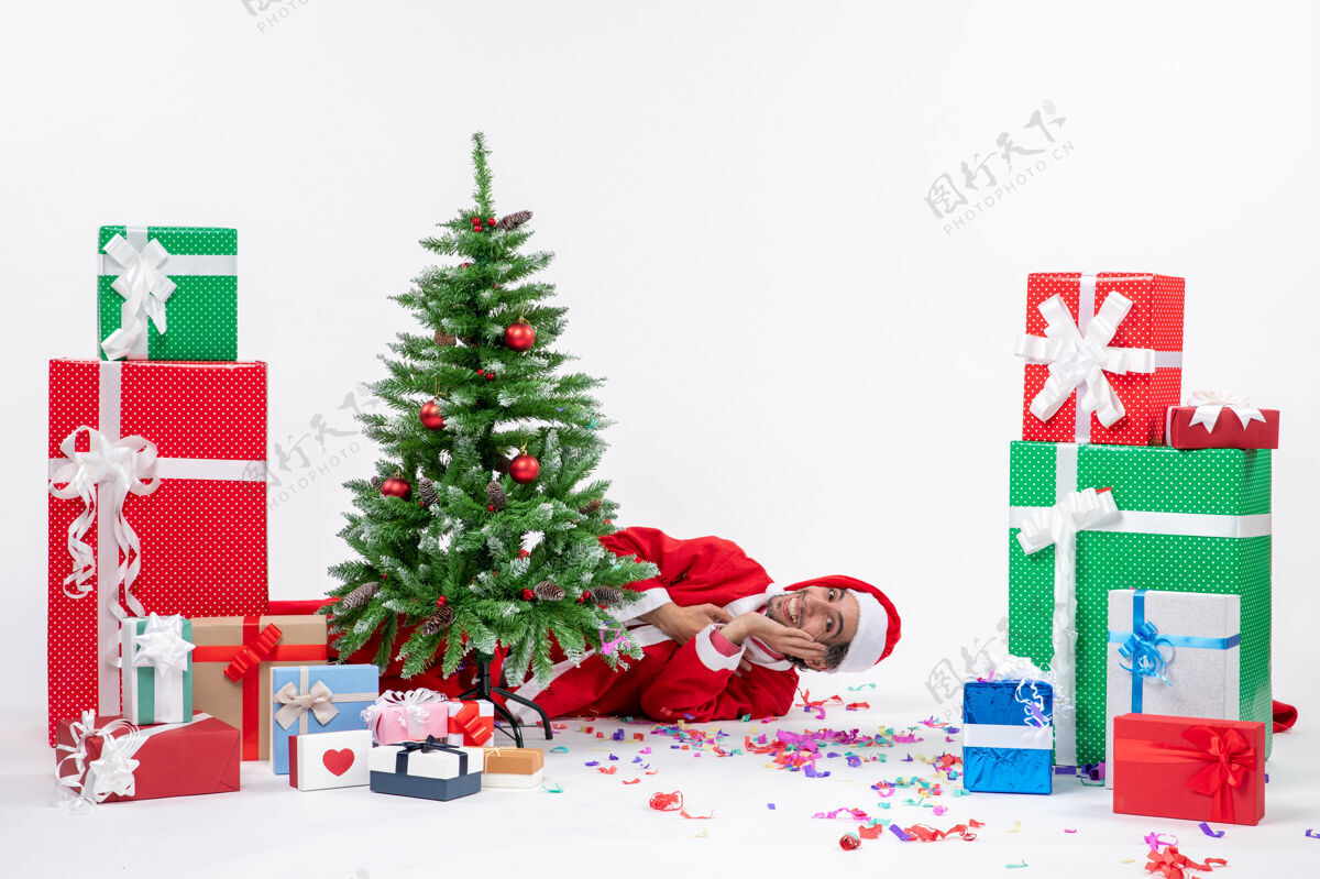 节日圣诞老人躺在圣诞树后面 在白色背景上有不同颜色的礼物 圣诞气氛喜庆礼物股票礼物