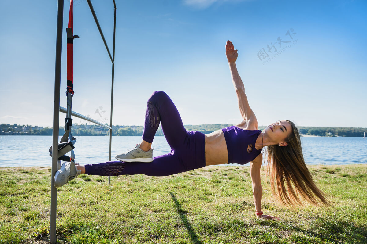 训练年轻苗条的女人在户外用健身带做悬吊训练锻炼吊索肌肉