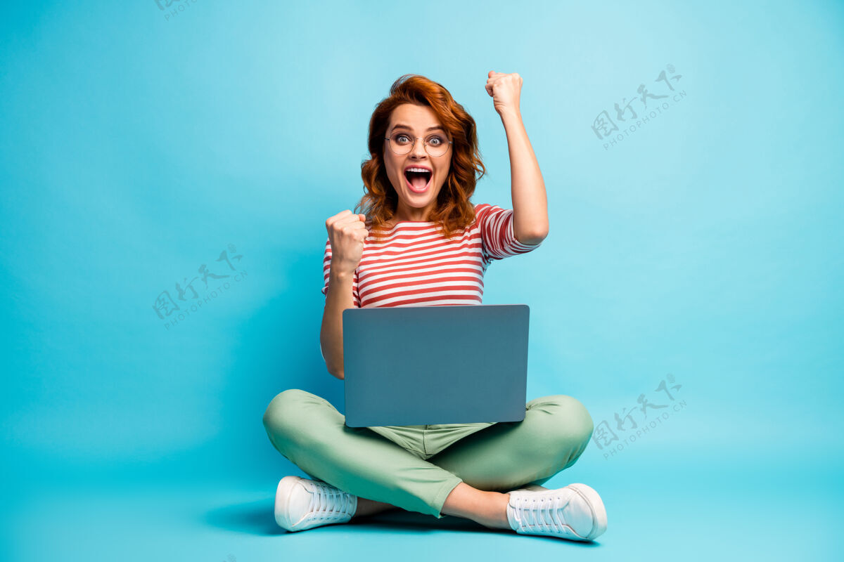 喜悦全尺寸照片疯狂酷聪明女人坐双腿交叉工作电脑完成她的项目尖叫耶举起拳头穿绿白色套装运动鞋蓝色隔离女性成功电脑