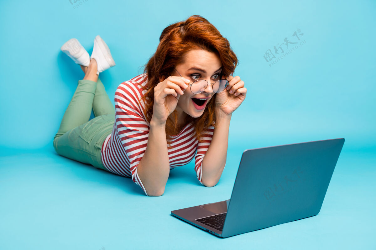 工作全长特写照片印象深刻的疯女人躺在地板上使用电脑阅读难以置信的博客通知尖叫哇omg穿白色好看套头衫孤立的蓝色乐趣自由职业者女性