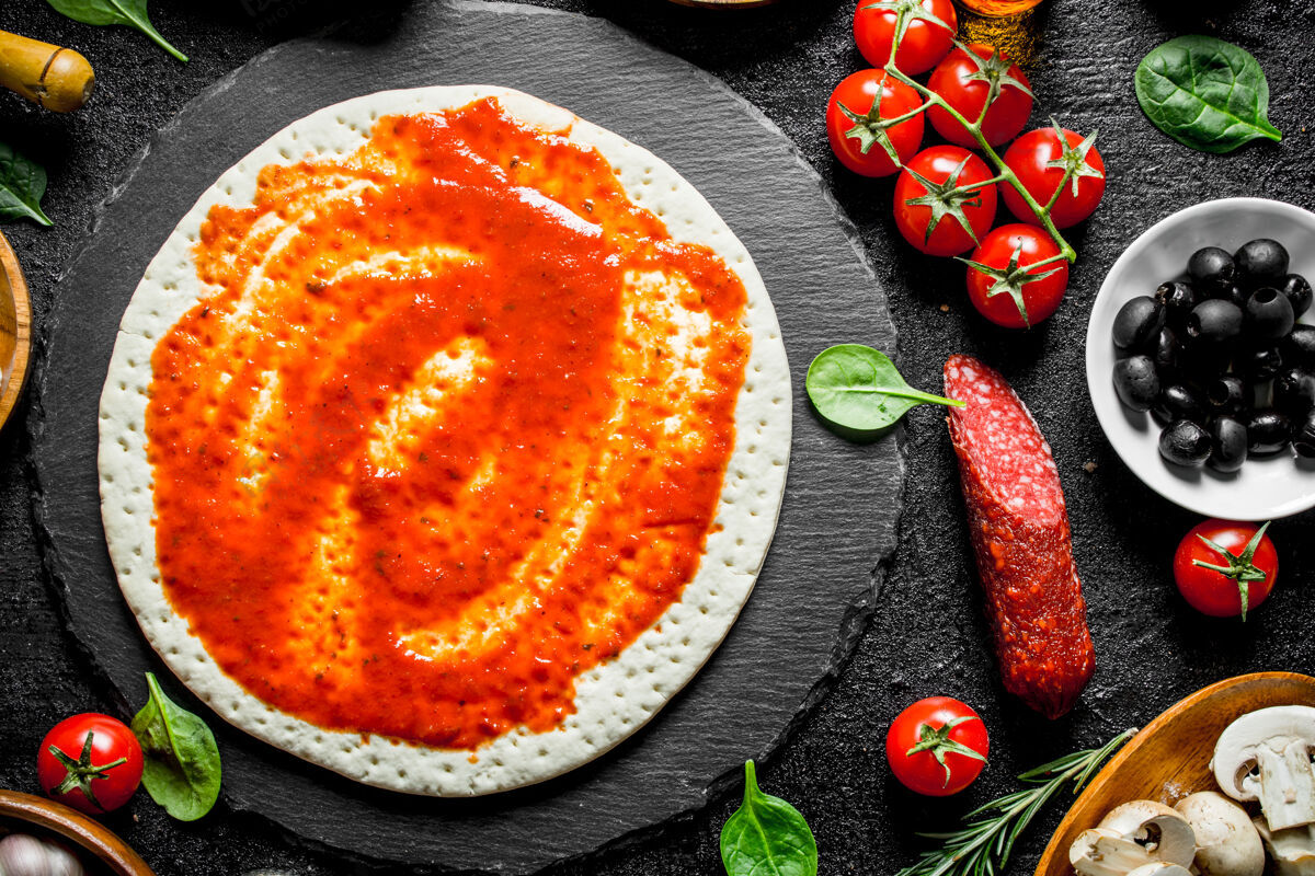 生的生披萨把番茄酱 香肠 马苏里拉和橄榄做成的面团放在黑色的乡村餐桌上自制意大利香肠食谱
