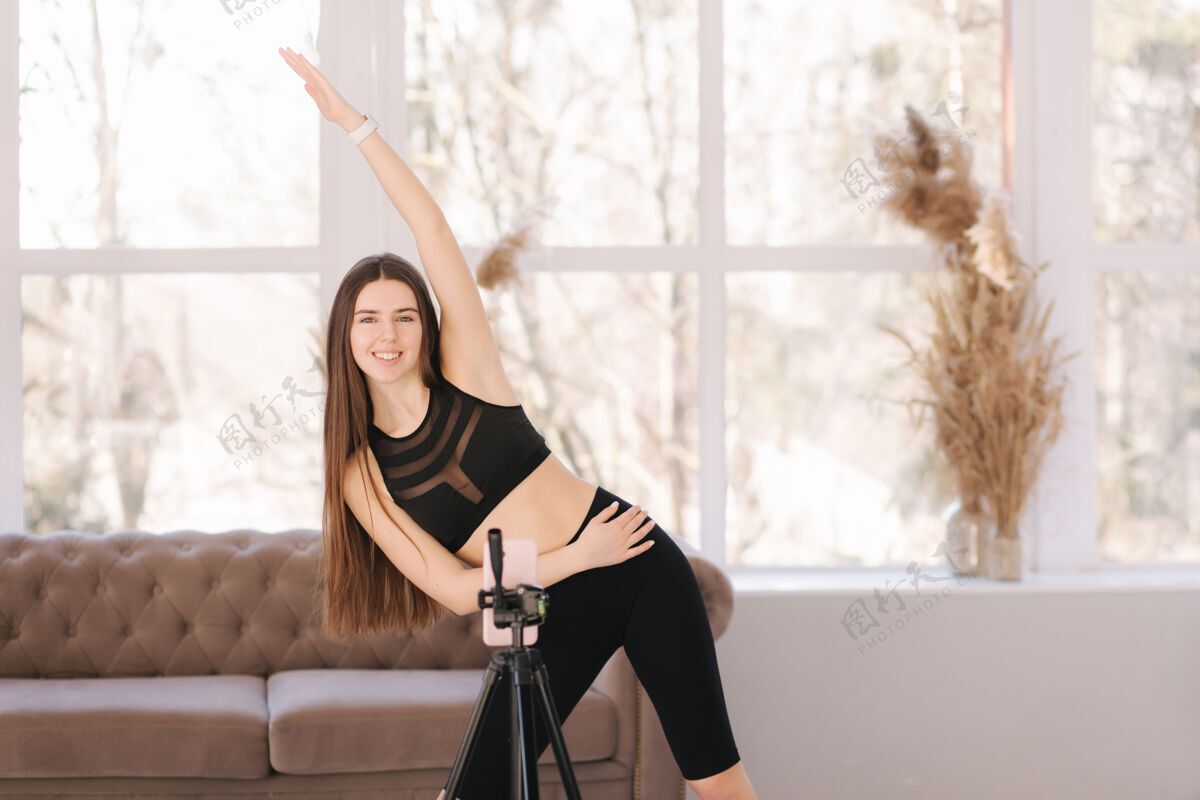 健身女孩年轻的女运动员博主在balcksportswear拍摄视频 因为她在家里客厅锻炼房子健康运动员