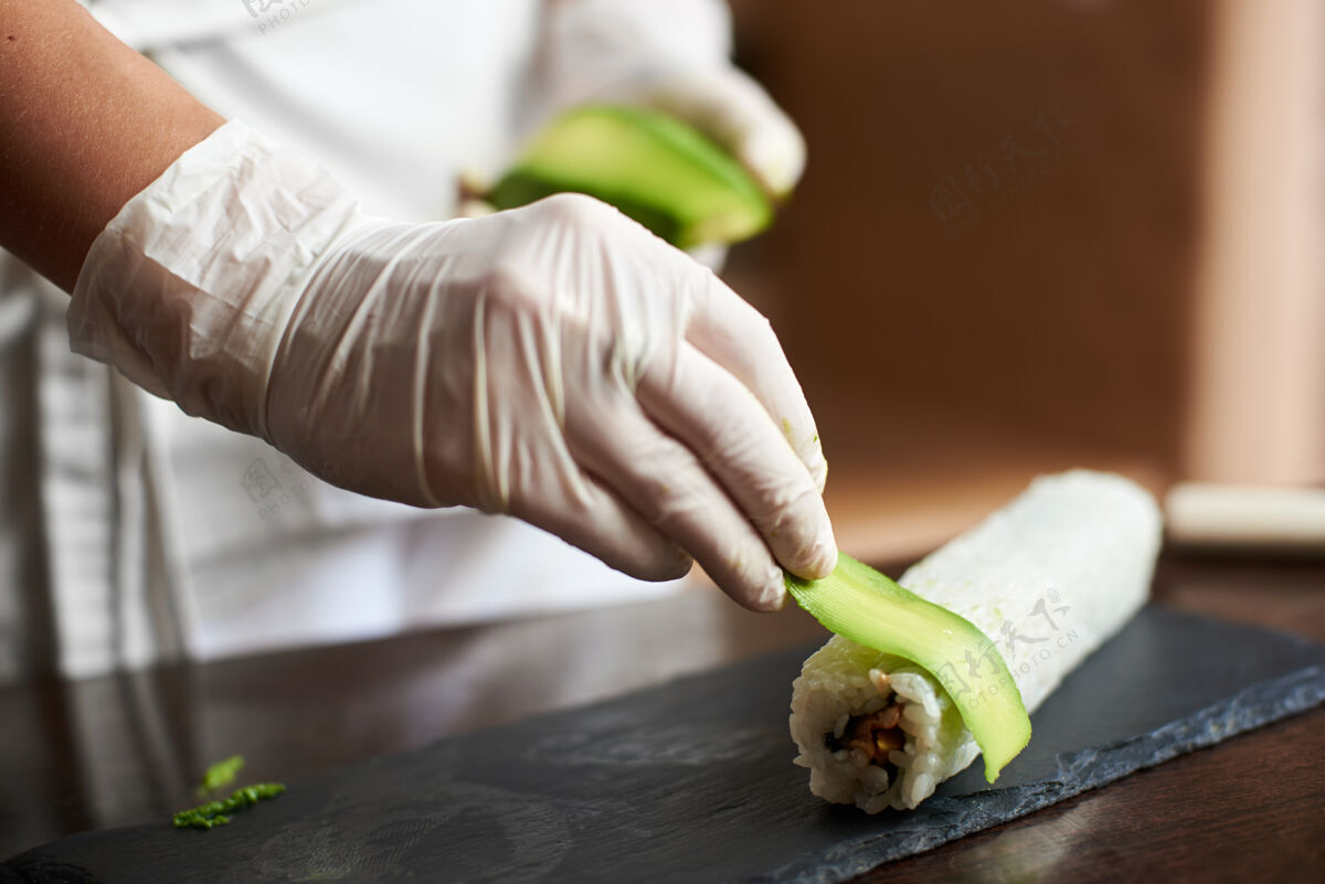 亚洲特写镜头的过程中准备滚动寿司手在手套装饰与切片鳄梨卷厨师切片控股