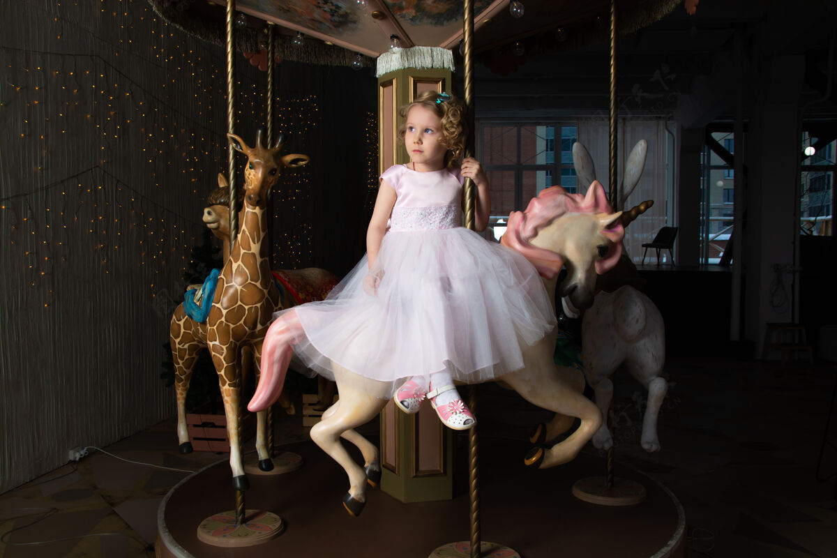 快乐一个穿着粉色裙子 戴着皇冠的女孩和一匹白色小马坐在旋转木马上宝贝快乐兔子