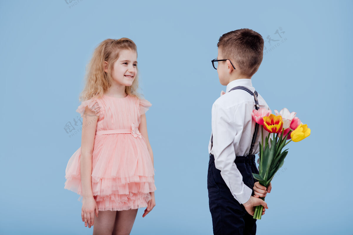 惊喜两个小孩 一个男孩拿着花 一个女孩穿着粉红色的衣服 孤零零地站在蓝色的墙上花束快乐裙子