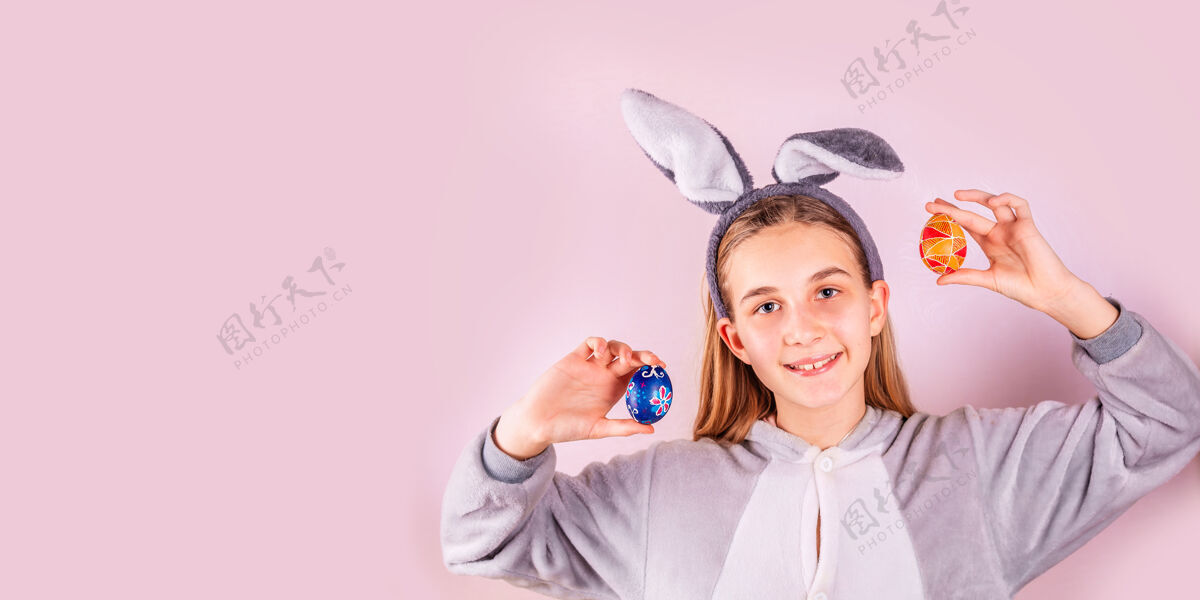 粉红色头上戴着兔子耳朵 粉红色背景上有彩色鸡蛋的女孩快乐的孩子乐趣可爱女孩