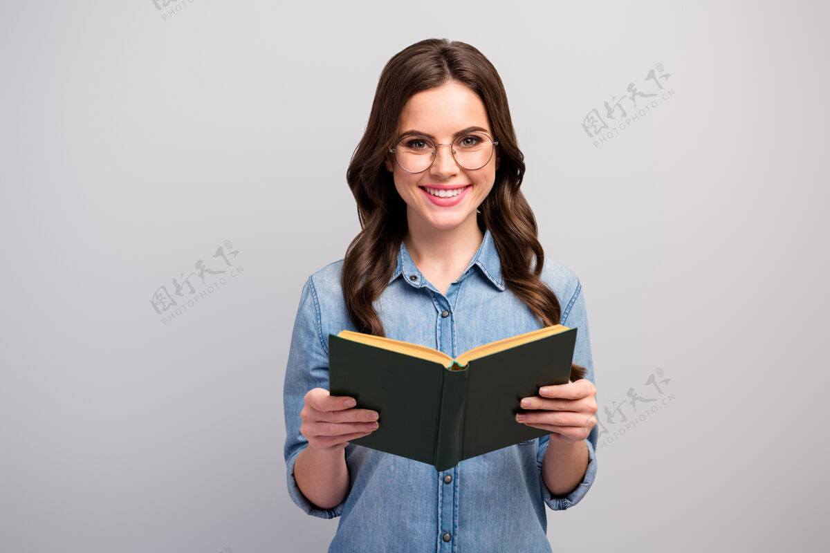 年轻照片中的俏皮搞笑的商务女士握着书的手读者牙牙学语笑容满面好心情穿眼镜休闲牛仔裤牛仔衬衫孤立的灰色手日记休闲