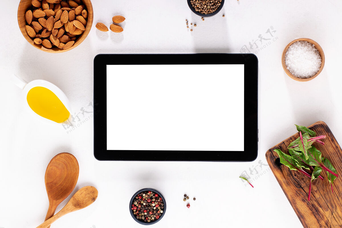 烹饪数字平板电脑 白色桌面上有空白屏幕 有香料 油 纸板 盐和坚果在线数字平板电脑桌子