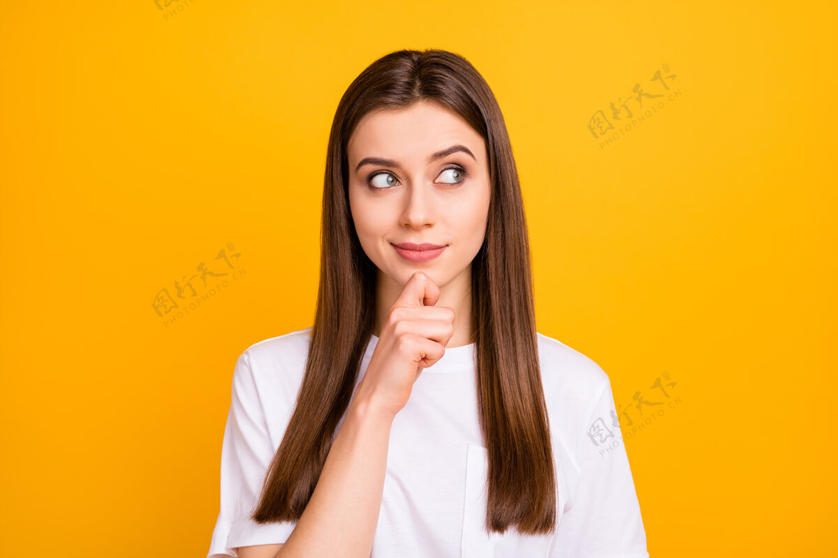 思想照片中的美女长发造型侧面空旷的空间看到有趣的广告横幅手指放在下巴上穿休闲白色t恤隔离鲜艳的黄色墙壁思考女人下巴