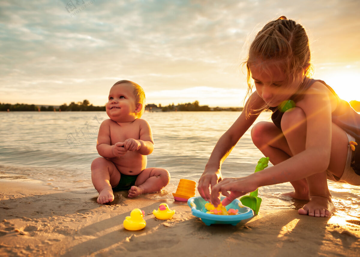 乐趣侧视图：可爱的小宝宝和小橡皮黄鸭子在蓝色的小水池里玩耍 和姐姐坐在沙滩上洗澡一起鸭子