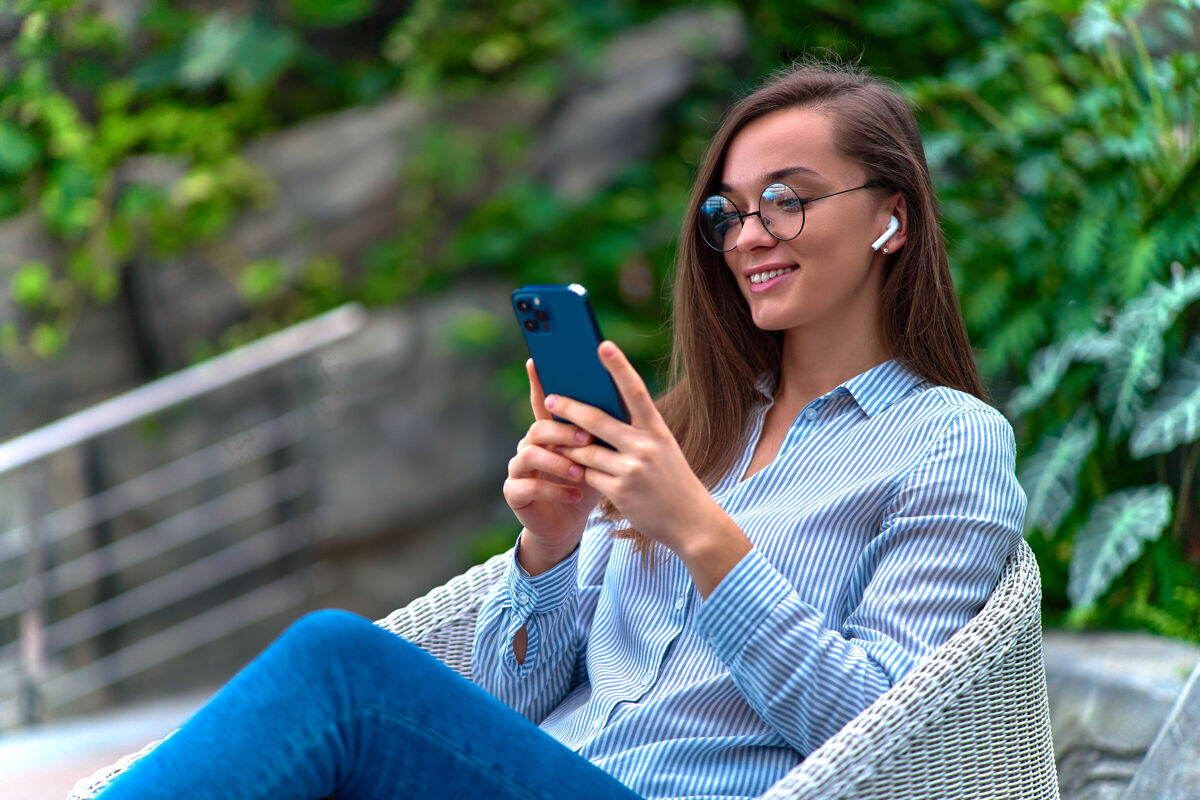 手现代快乐休闲聪明的千禧一代女性戴着无线耳机用智能手机远程聊天和上网浏览打字通信电话