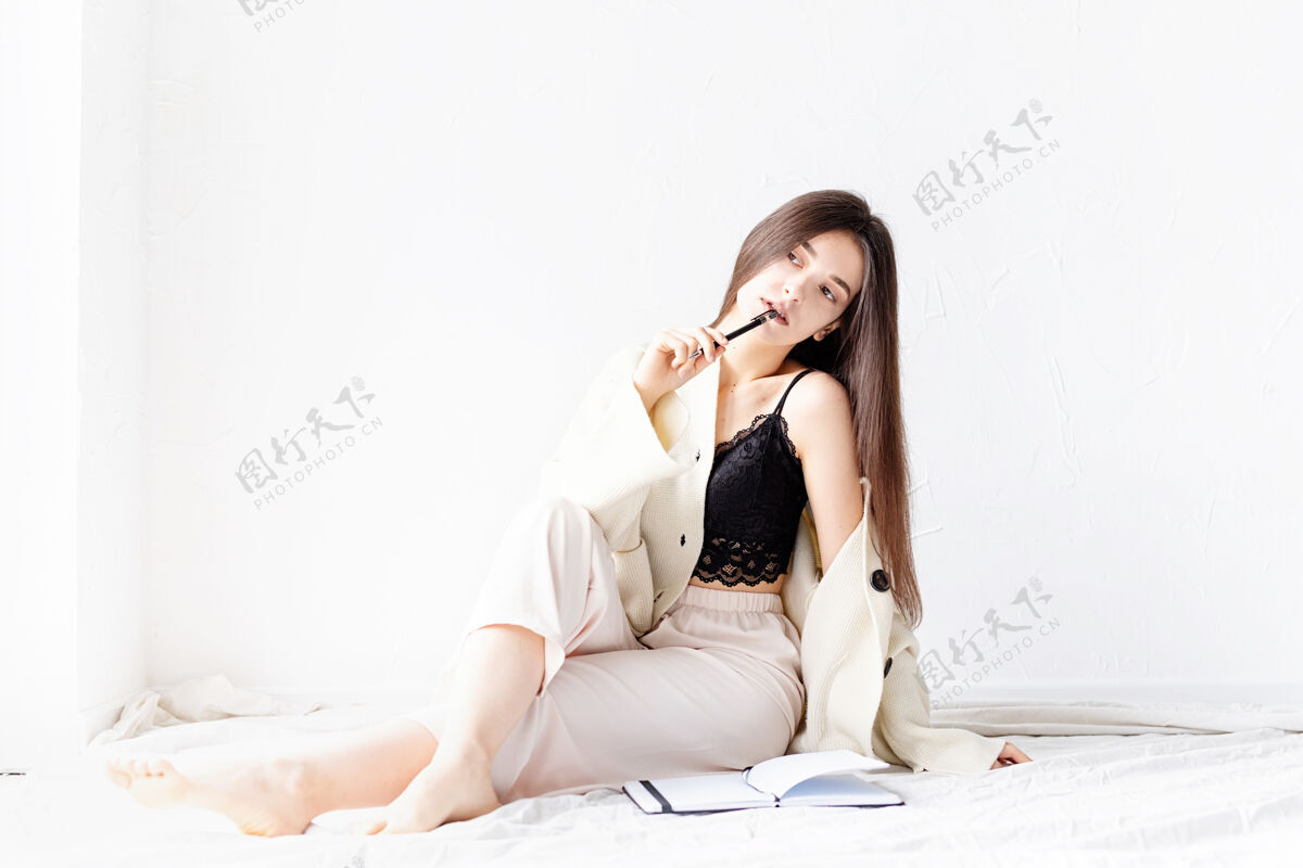 工作场所穿着舒适家居服的性感美女坐在地板上写笔记 思考钢笔学习舒适