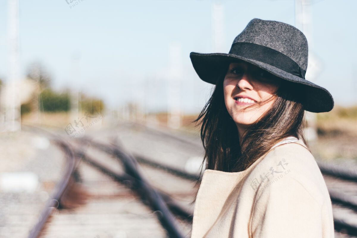 纽约在废弃的铁轨上穿着米色雨衣戴着帽子的快乐女人行李火车头铁路