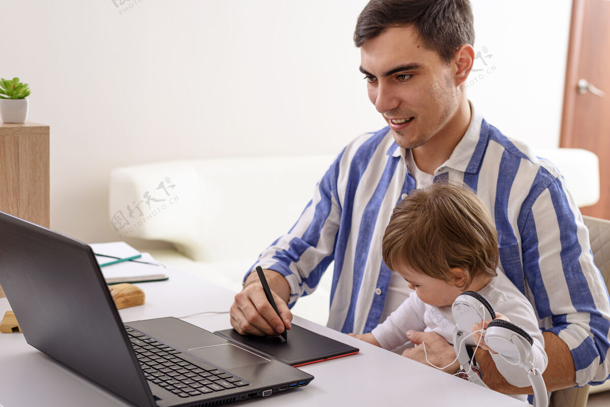 无线爸爸抱着孩子坐在膝上 在家里用笔记本电脑远程工作留在家里房子安全