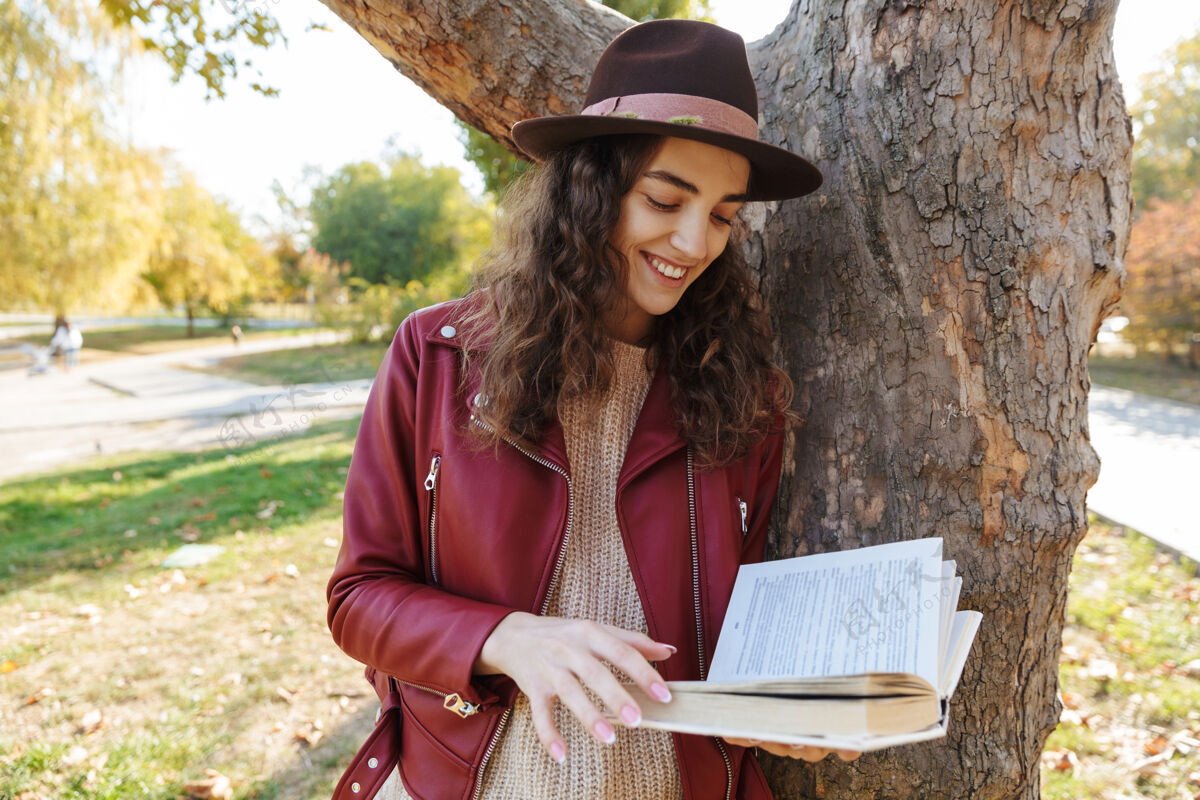 魅力一个美丽可爱的女人站在公园附近的树上看书的照片白种人年轻肖像