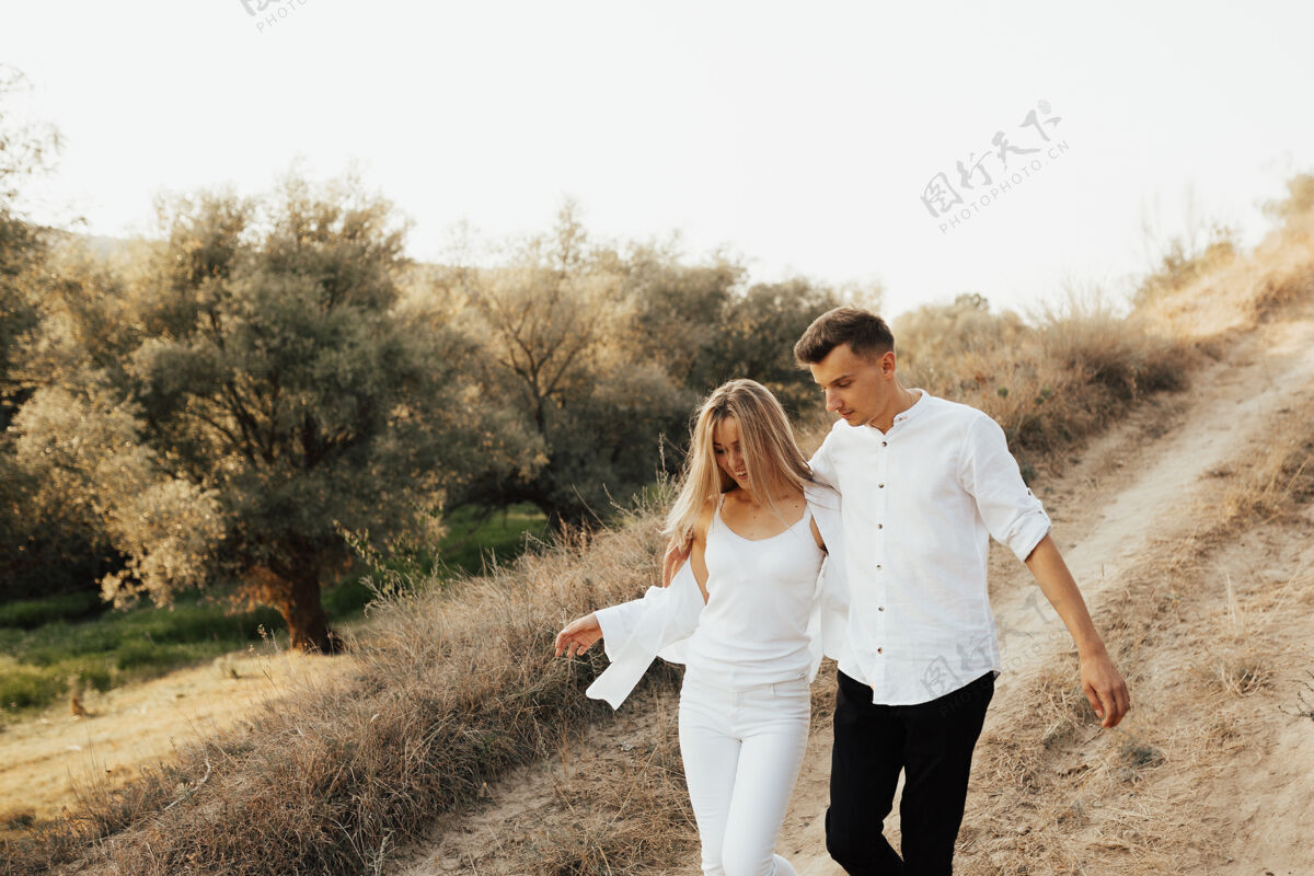 户外一对穿着白色衣服的情侣在夏日公园散步 拥抱 面带微笑举行一起乡村