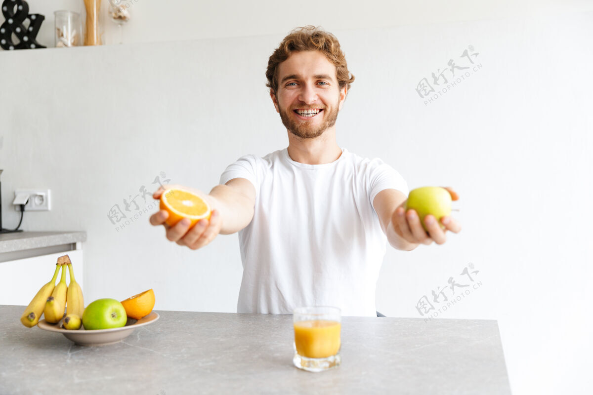 白种人一位快乐的留着胡子的年轻人在家里的桌子旁拿着水果的照片成人文学早餐