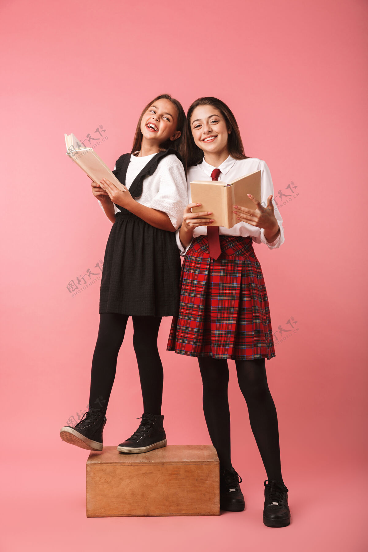 优雅两个穿着校服的开朗的女生孤立地站在粉红色的墙上 手里拿着书学校教育学习