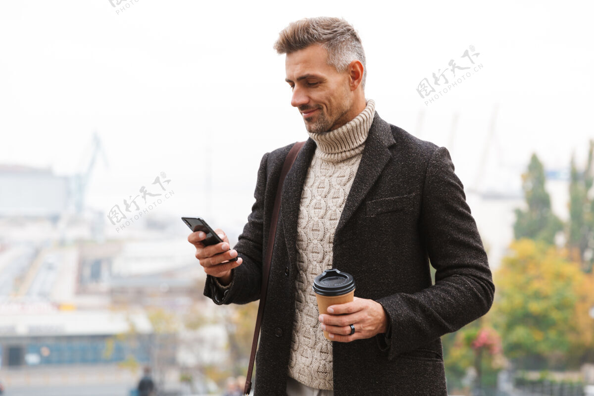 白种人帅哥穿着夹克走在户外 端着一杯外卖咖啡 用手机休闲茶饮料