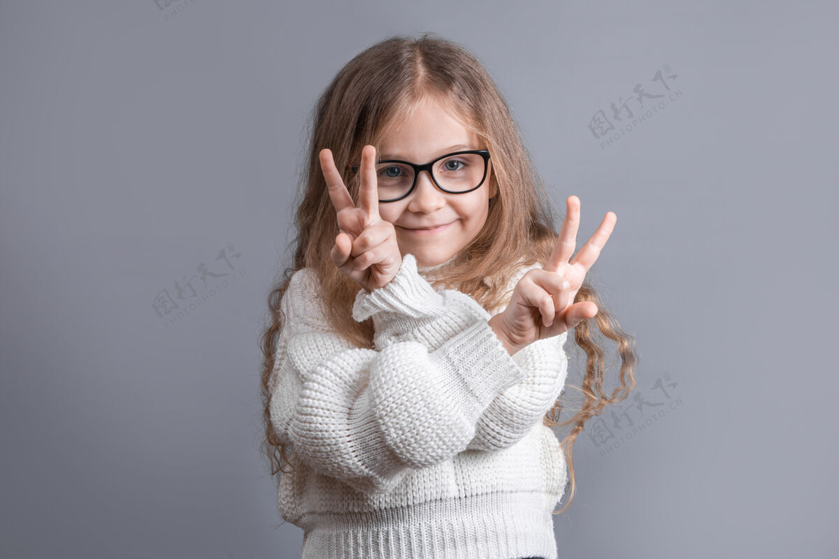 可爱一个年轻漂亮的金发小女孩的肖像 穿着毛衣 上面有v字标志胜利女人手指
