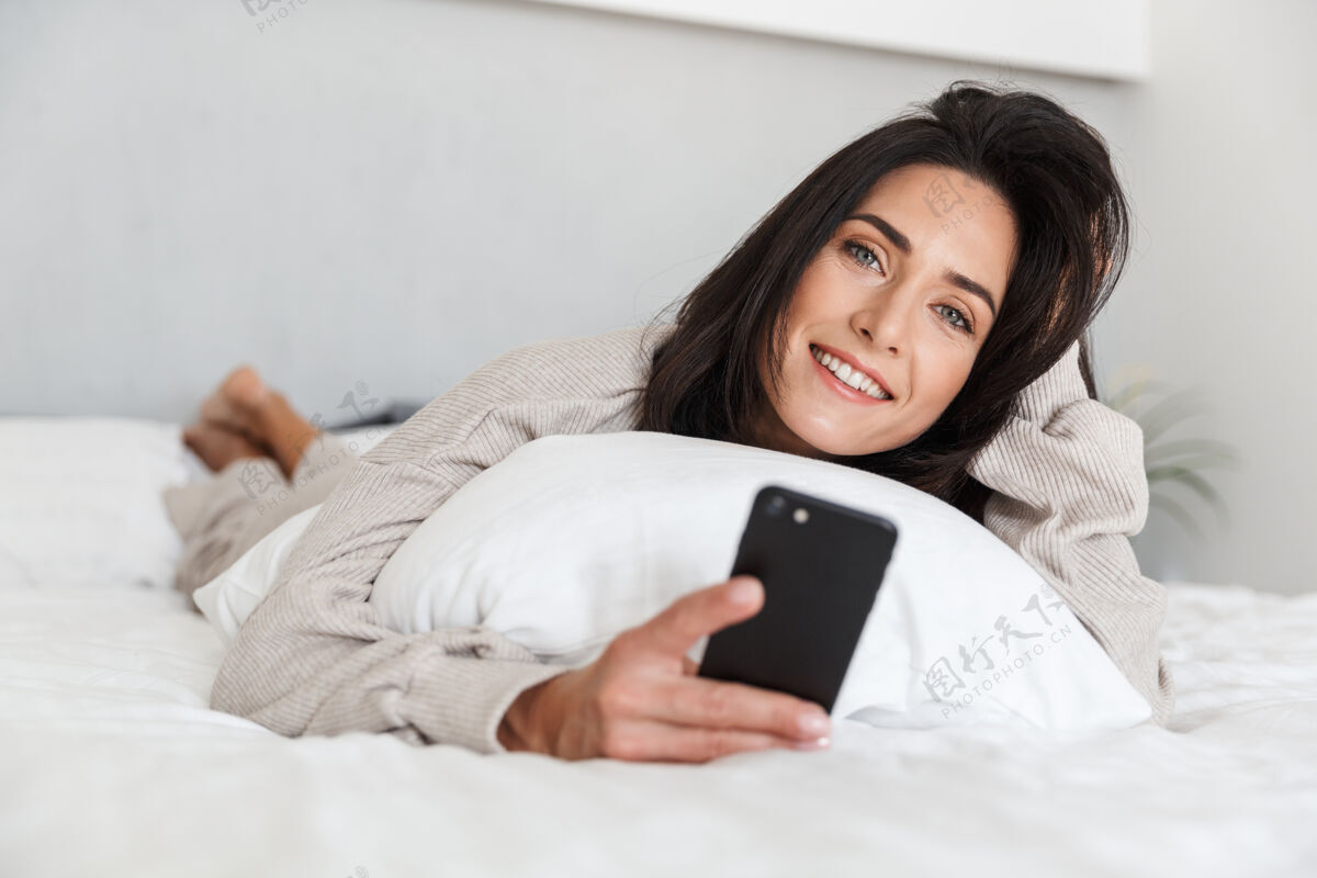 舒适一张30多岁的中年妇女在明亮的房间里躺在床上用手机的照片沙发床愉快