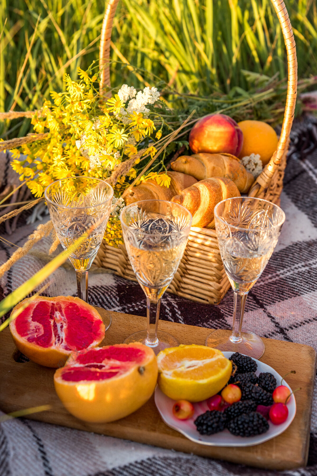 野餐野餐篮里有两个牛角包 葡萄柚 橘子 浆果和香槟 在绿色阳光普照的草坪上阳光休闲周末