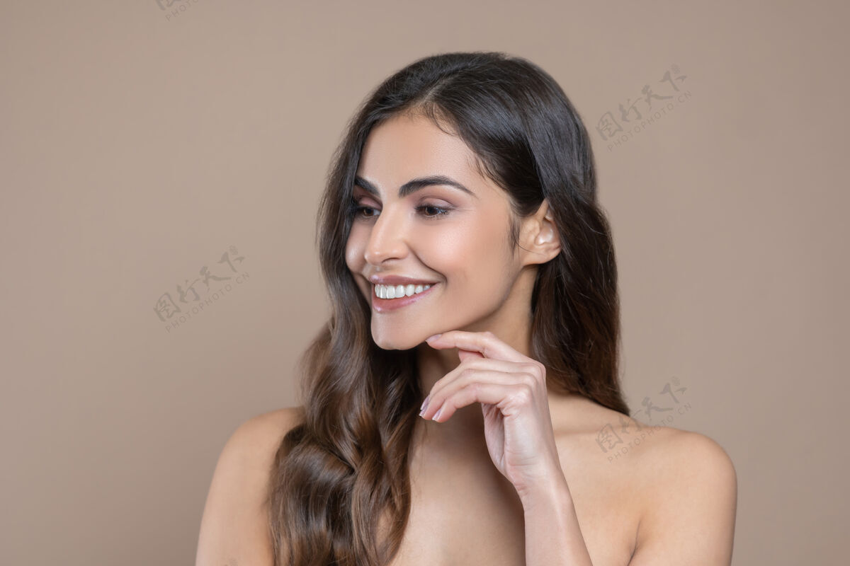 腰向上女性看起来很漂亮在室内 微笑的女人一边看着一边用手指碰下巴化妆卷曲半裸