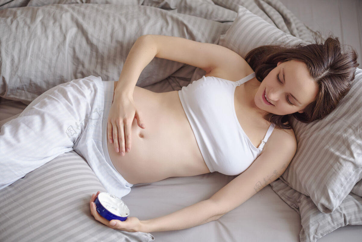 皮肤俯视图怀孕的黑发女人在怀孕期间躺在床上照顾皮肤 涂抹乳霜腹部生活方式药物女人