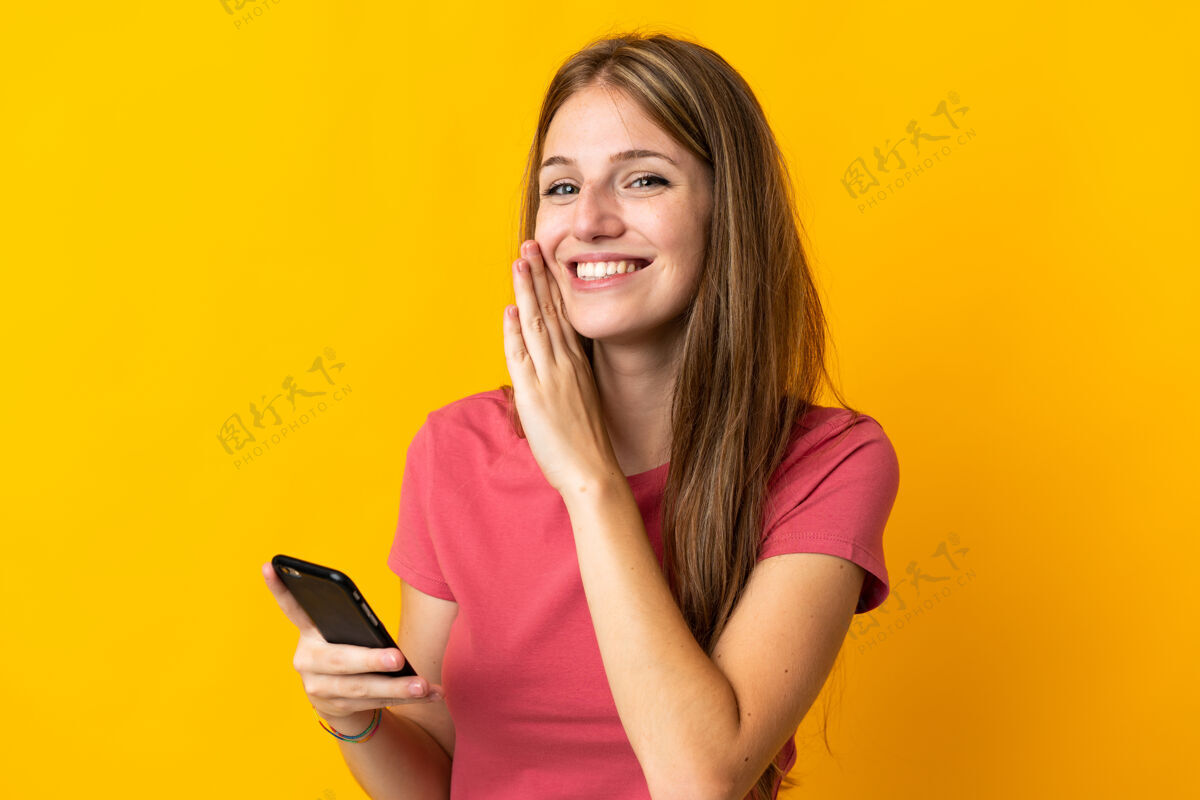 女孩年轻女子用手机隔离在黄色背景上窃窃私语什么的通信电话对话