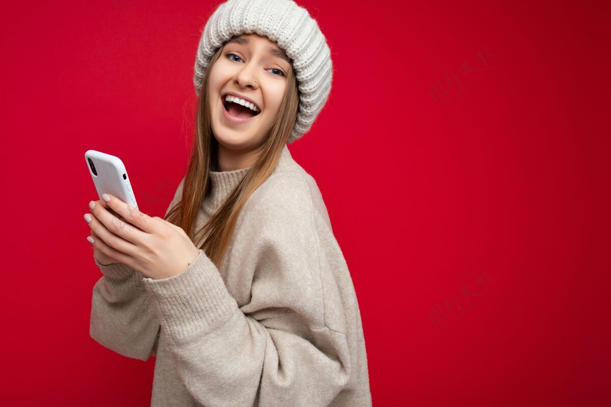 发送照片中的年轻女子穿着休闲时尚的衣服 独自站在背景上 拿着复印件 用手机看着相机移动温暖的毛衣使用