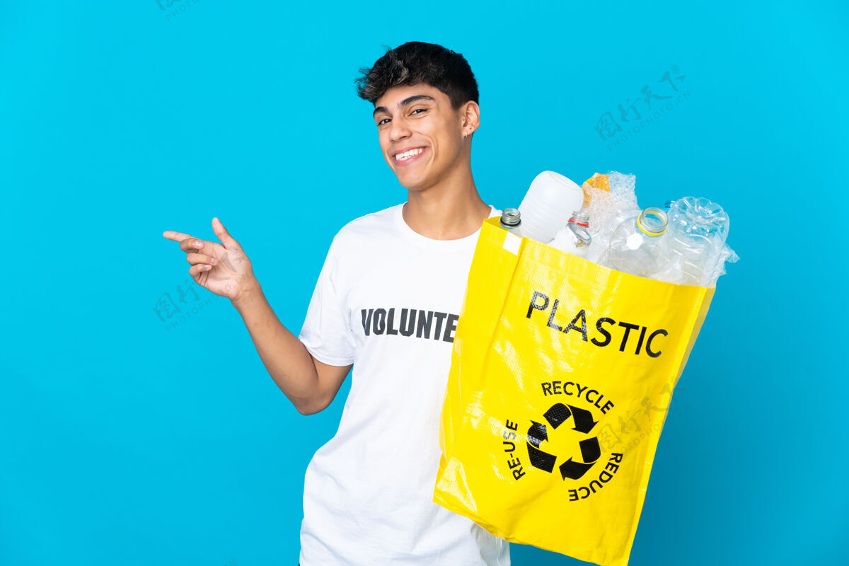 介绍拿着一个装满塑料瓶的袋子 在蓝色的墙上用手指着一边 展示一个产品塑料再利用指