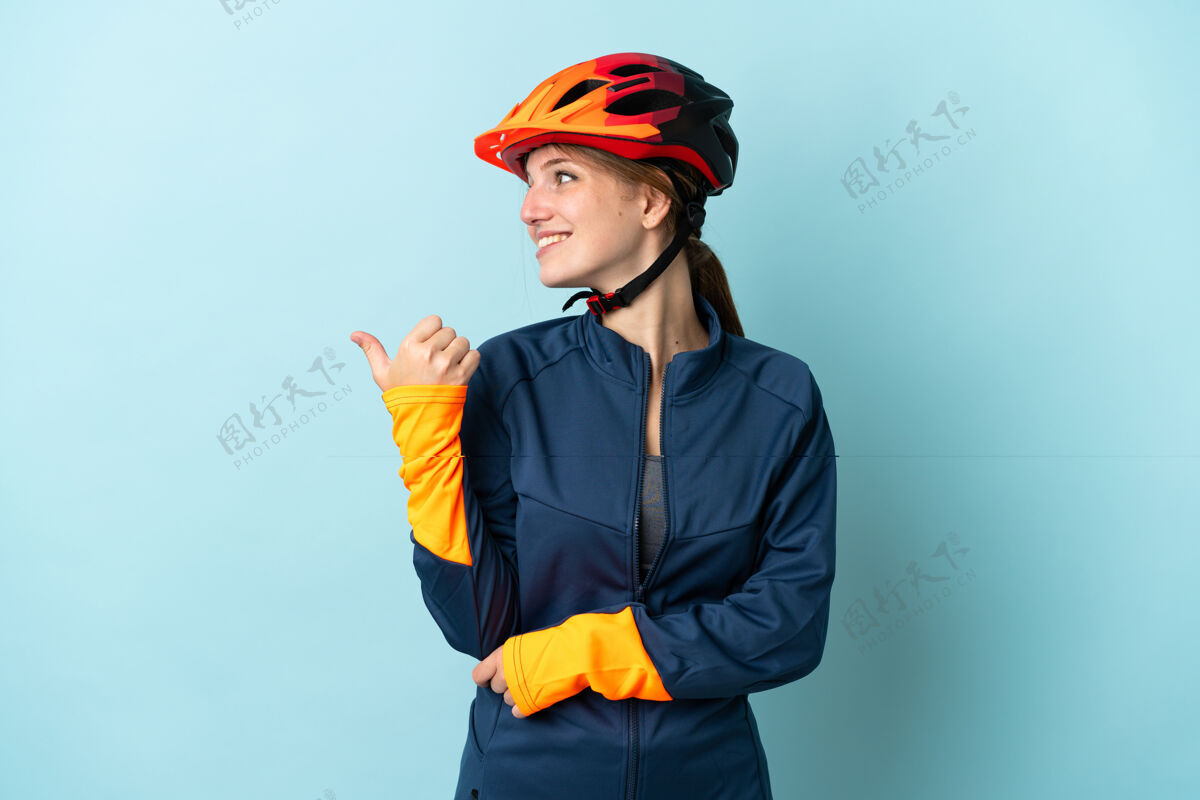 看年轻的女自行车手孤立在蓝色的背景下指着旁边的产品介绍女性女孩指着