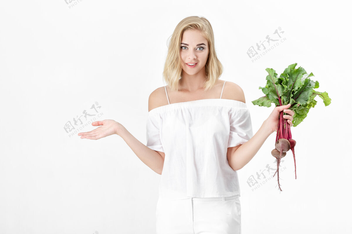 维生素一位穿着白色上衣的金发美女手持一根长着绿叶的甜菜根背景.健康还有维生素烹饪自然举行