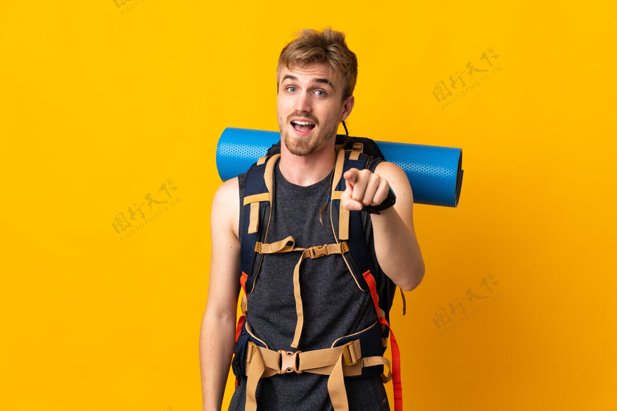 背包年轻的登山者背着一个大背包 独自站在黄色的背景上 惊讶地指着前面男性远足帅哥