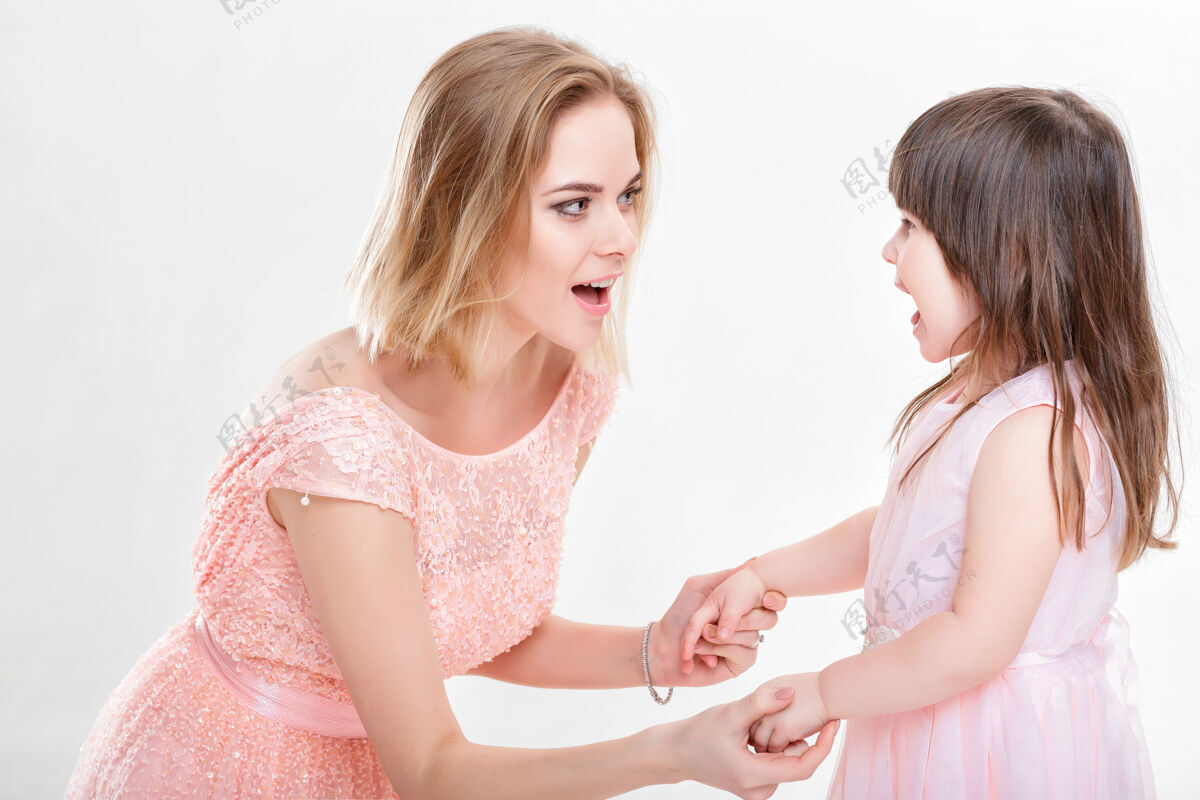 年轻金发妈妈穿着粉色连衣裙安慰女儿灰色公主背景宝贝她在哭甜蜜女性金发