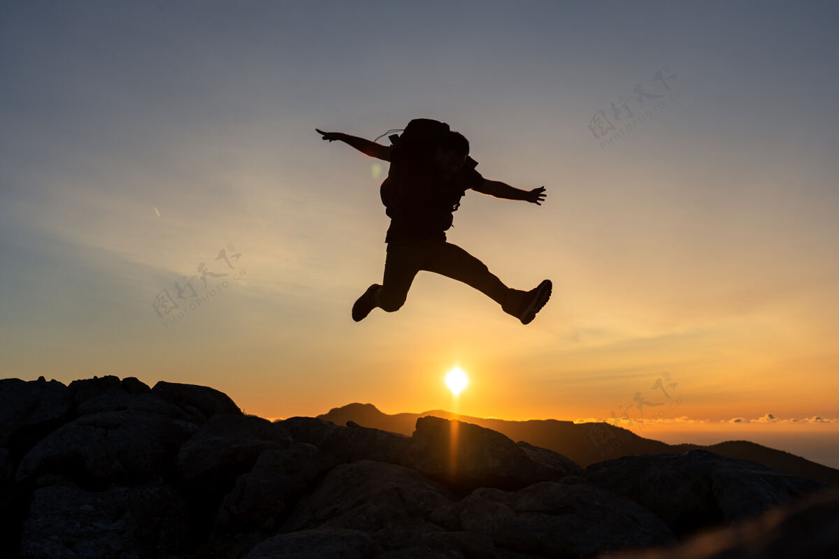 人在山顶的徒步旅行者 背着大背包 在夕阳下跳跃视角态度山脉